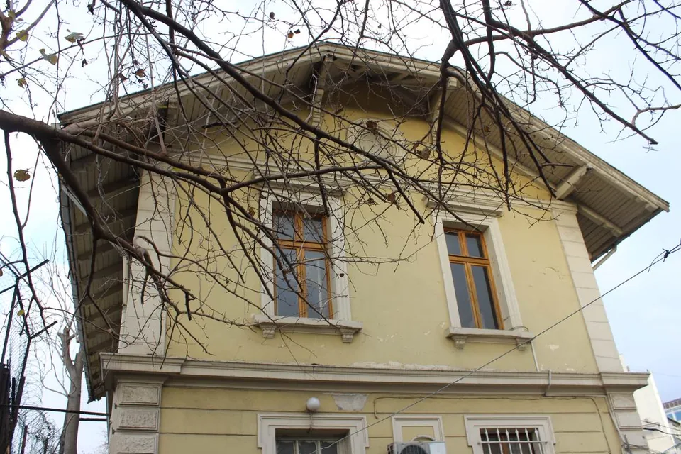 Yenikapı lojman binası, sarı sıvalı cephe, ahşap doğramalı pencereler ve önündeki ağaç dalları